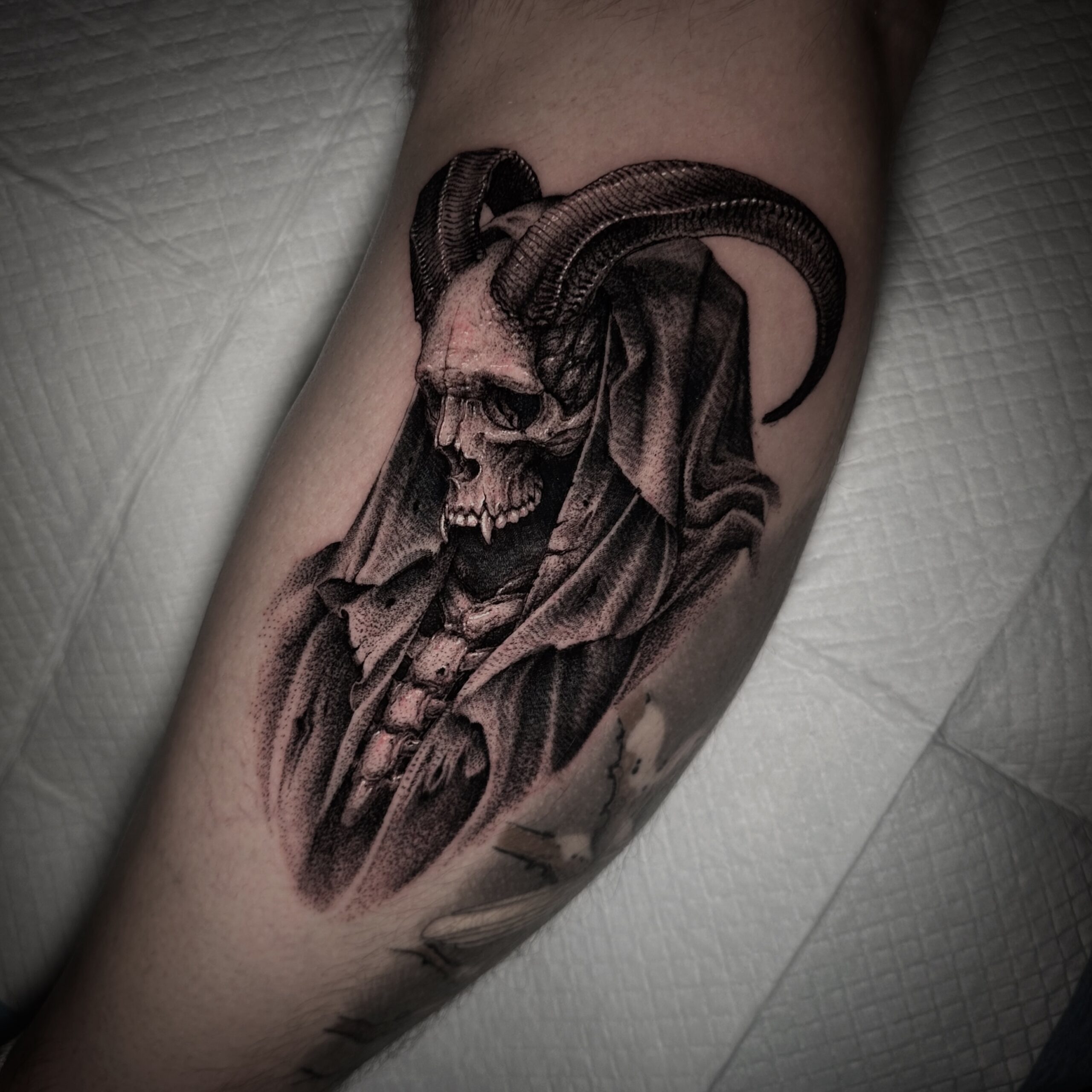 Blackwork tattoo van een gehoornde schedel in een kap op het onderbeen.