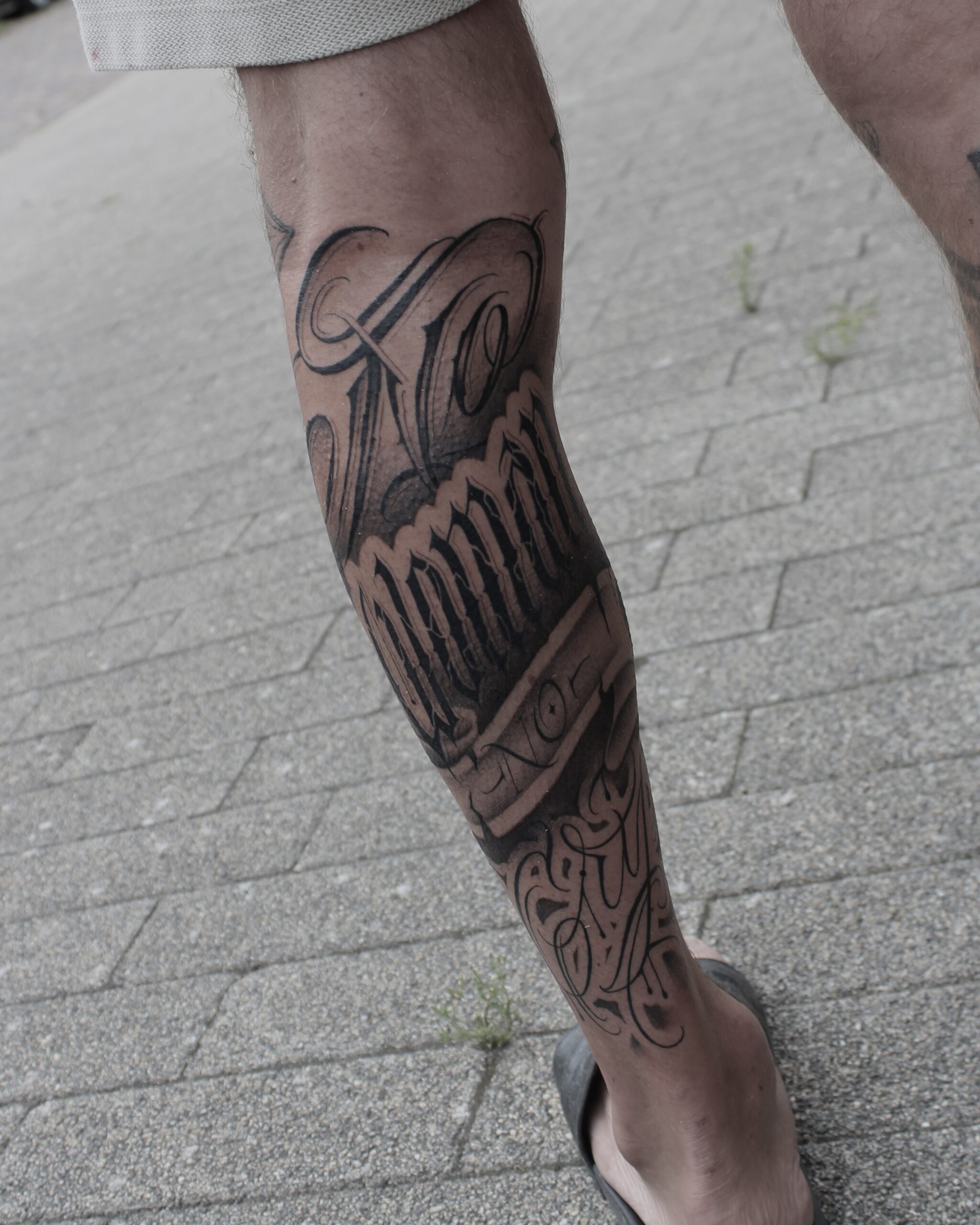Grote blackwork lettering tattoo op het onderbeen met de tekst 'Family'.