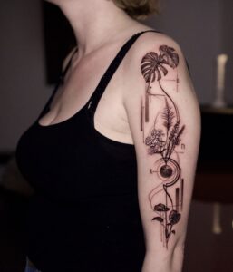 Fineline botanische en geometrische tattoo op bovenarm.