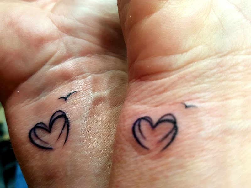 Twee bijpassende minimalistische hart en vogel tattoos op polsen.