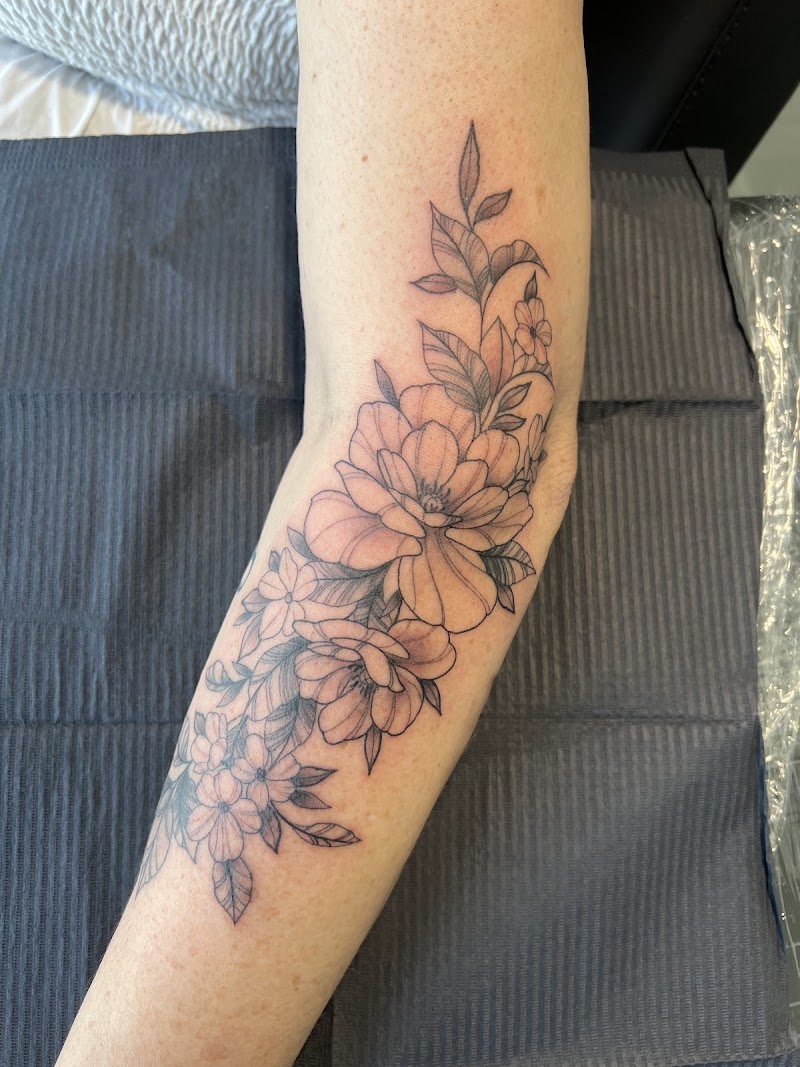 Fineline bloemen en bladeren tattoo op de onderarm.