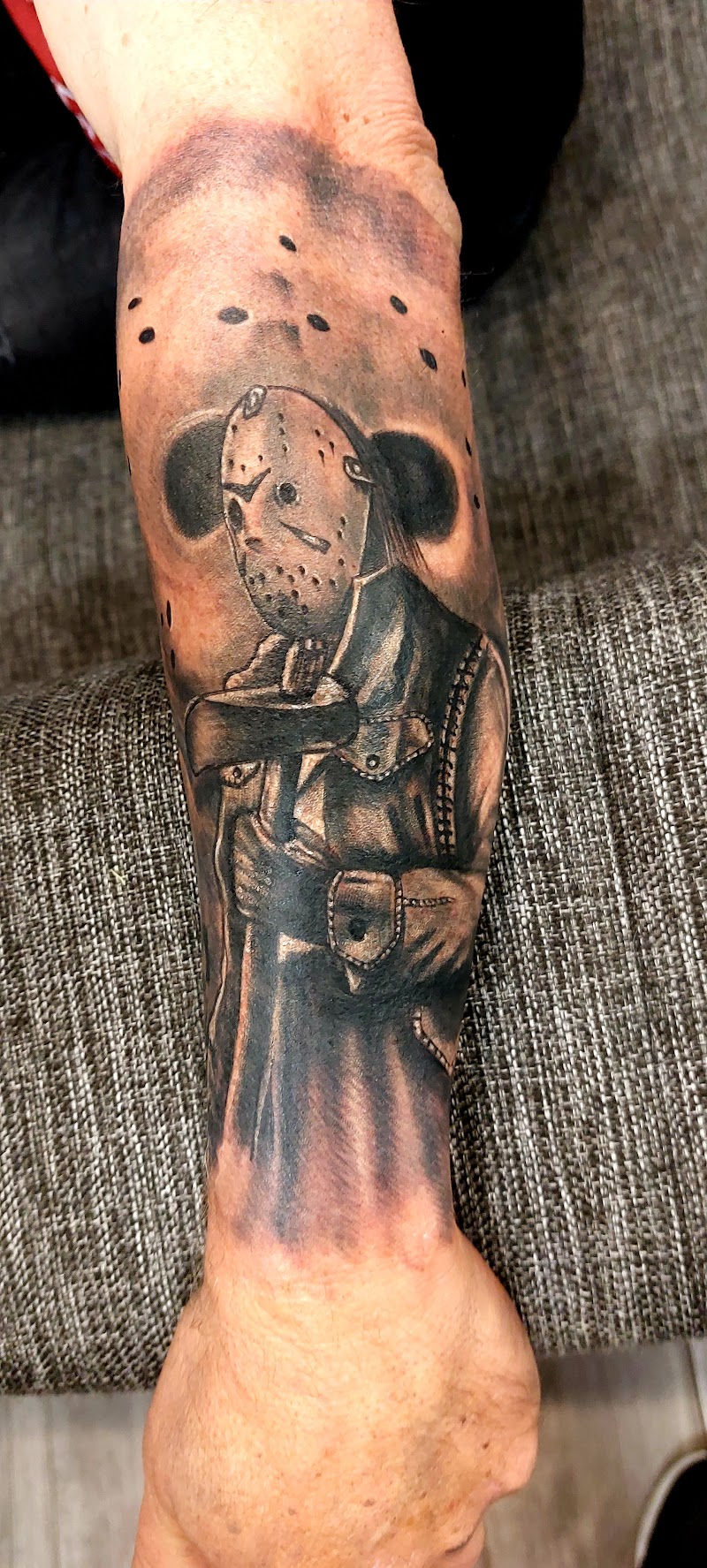 Realistische Jason Voorhees tattoo met masker en bijl op onderarm.
