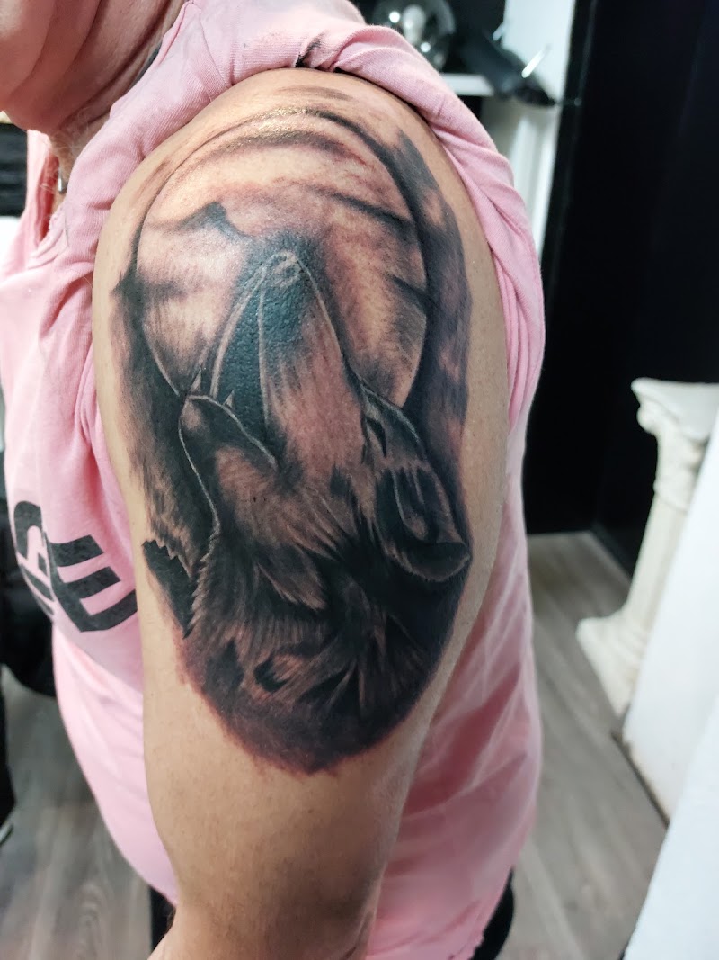 Blackwork tattoo van een huilende wolf voor een volle maan op de bovenarm.