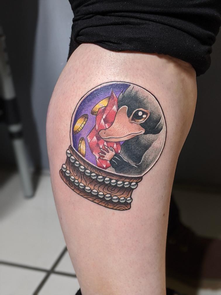 Kleurrijke Niffler in sneeuwbol met juwelen op onderbeen.