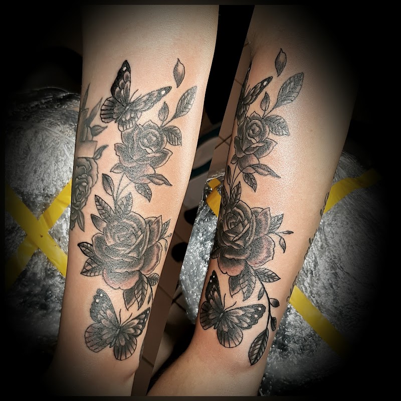 Zwart-wit tattoo van rozen en vlinders op beide onderarmen.