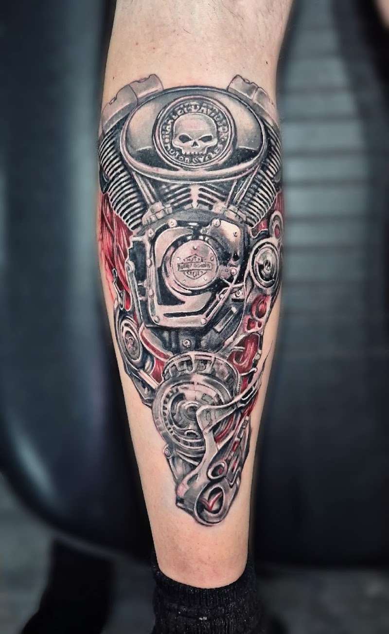 Biomechanische tattoo van een Harley-Davidson motorblok op een onderbeen.