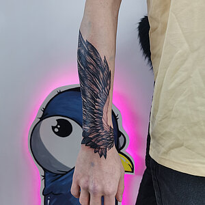 Gedetailleerde zwart-grijze vleugel tattoo op de onderarm.