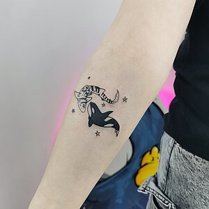 Kleine blackwork tattoo van een tijgerhaai en orka die samen zwemmen met sterretjes.