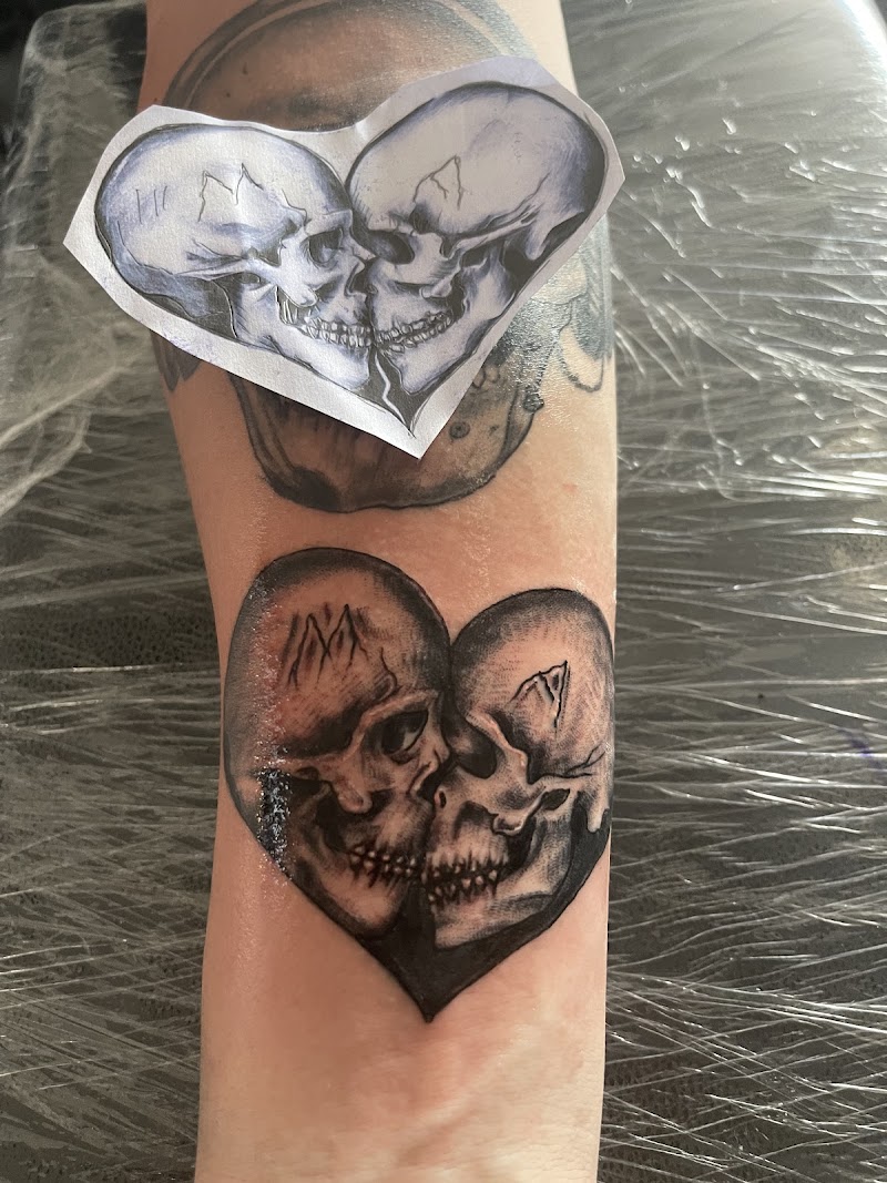 Zwart-wit tattoo van twee schedels die samen een hartvorm vormen op de onderarm.