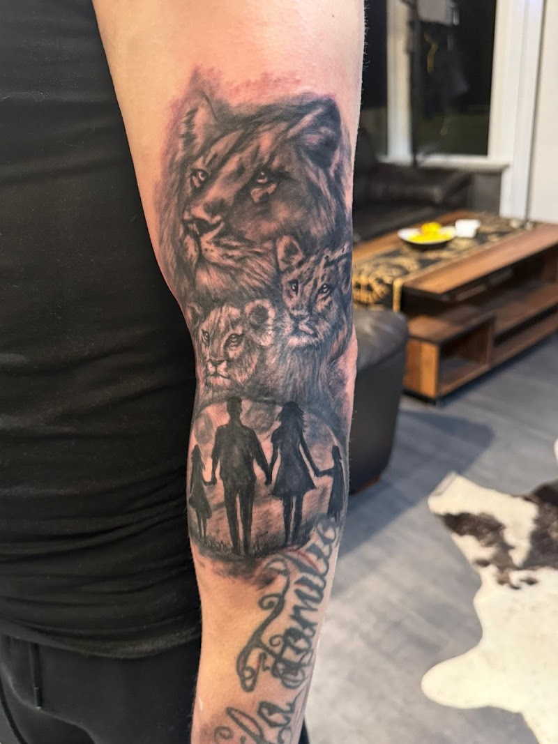 Zwart-wit tattoo van leeuwenfamilie, gezinssilhouet en tekst op arm.