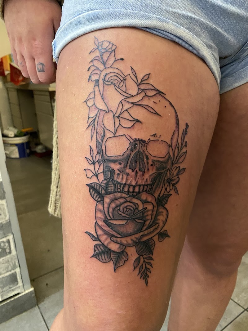 Illustratieve tattoo van een schedel met rozen op het bovenbeen.