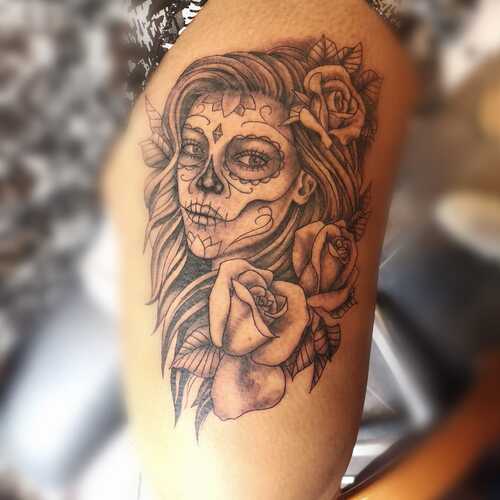 Zwart-wit tattoo van een Day of the Dead vrouw met rozen op het bovenbeen.