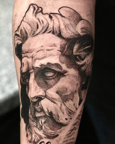 Zwart-wit tattoo van een klassiek standbeeld portret op de arm.