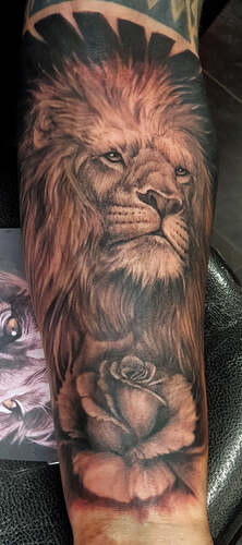 Realistische leeuwenkop met roos op onderarm.