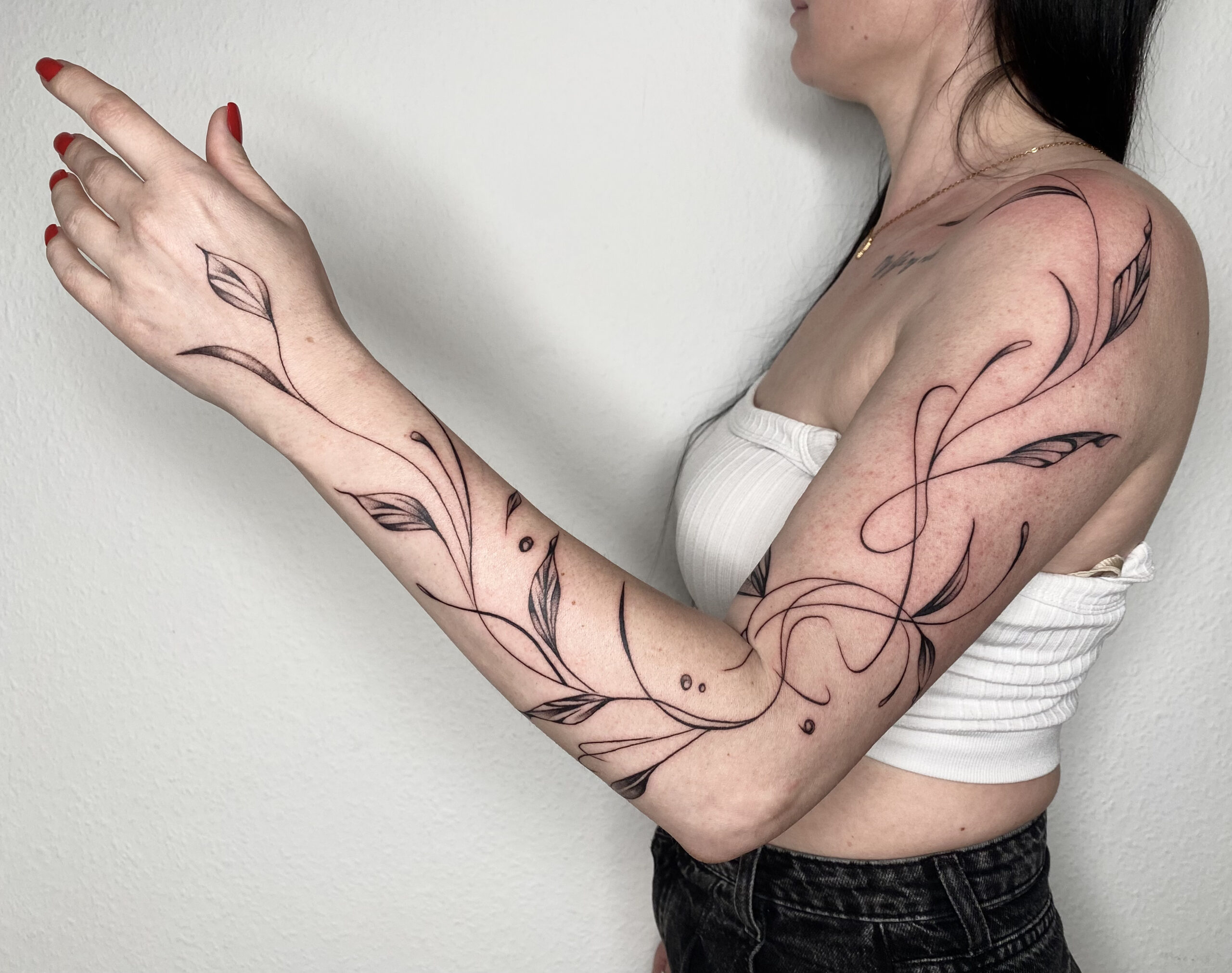 Elegante fineline tattoo van sierlijke bladeren en lijnen over de hele arm.