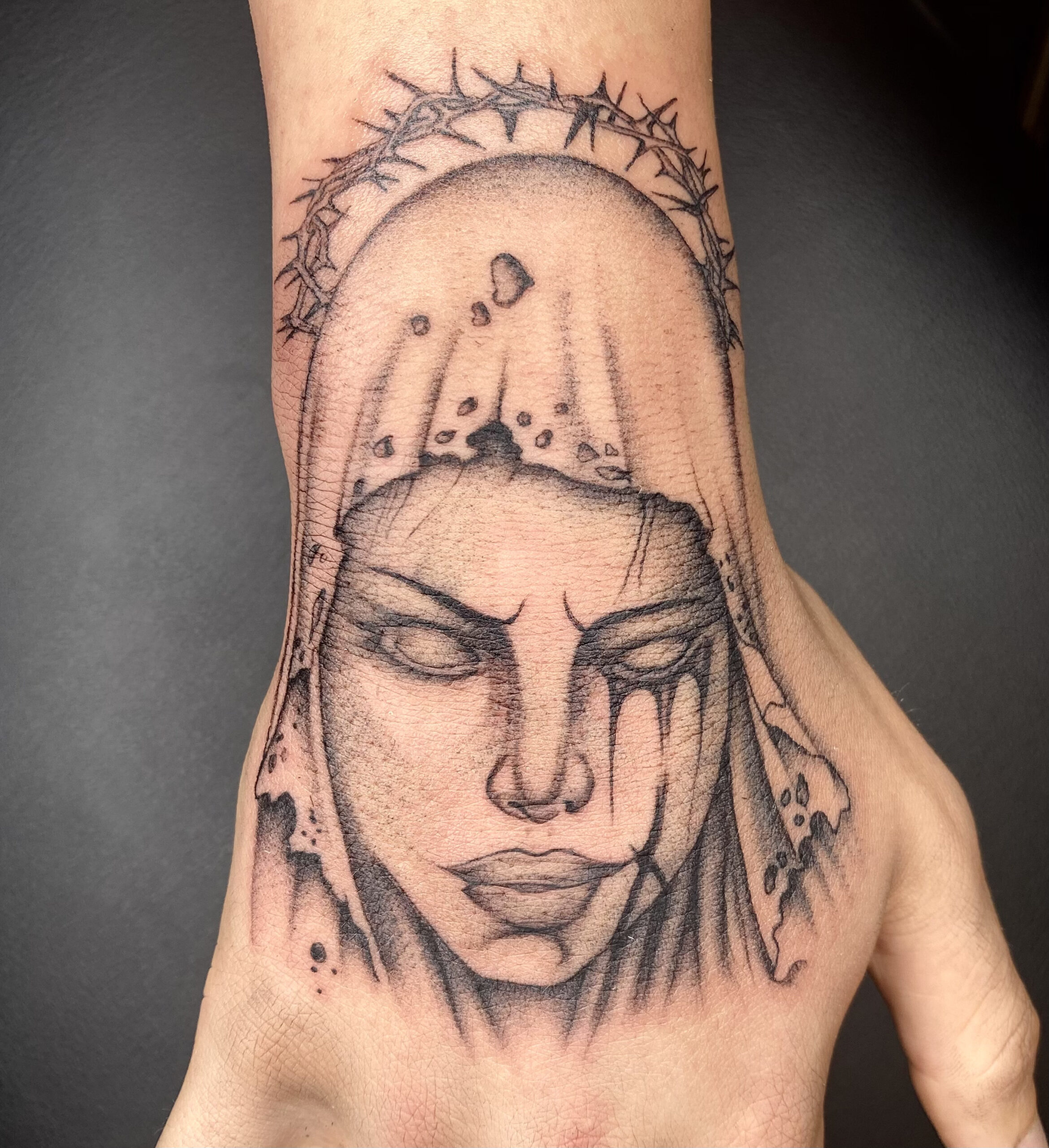 Blackwork tattoo van een huilende vrouw met doornenkroon op de hand.