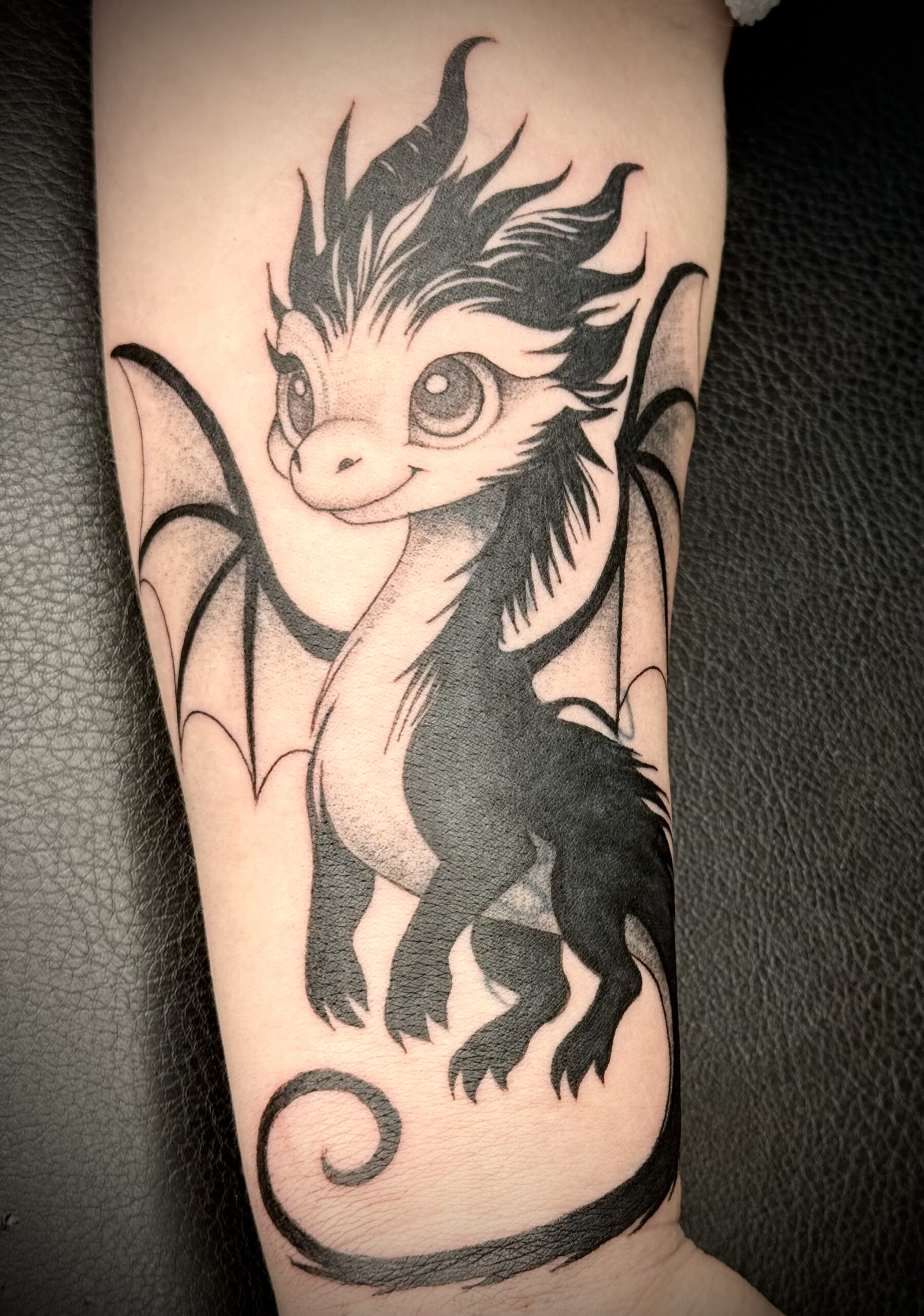 Schattige baby draak tattoo in blackwork stijl op de onderarm.