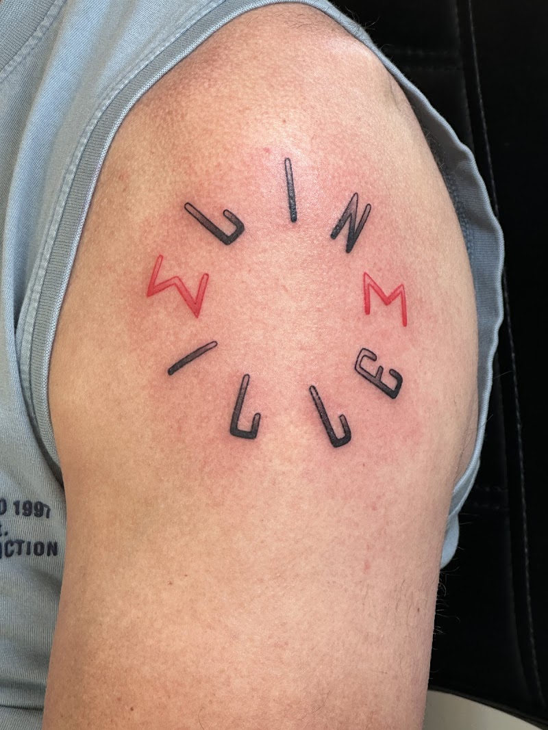 Cirkelvormige tekst tattoo met zwarte en rode letters op de schouder.