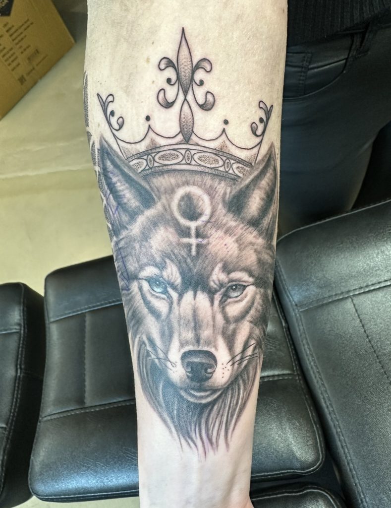 Blackwork wolf met kroon en vrouwensymbool op onderarm.