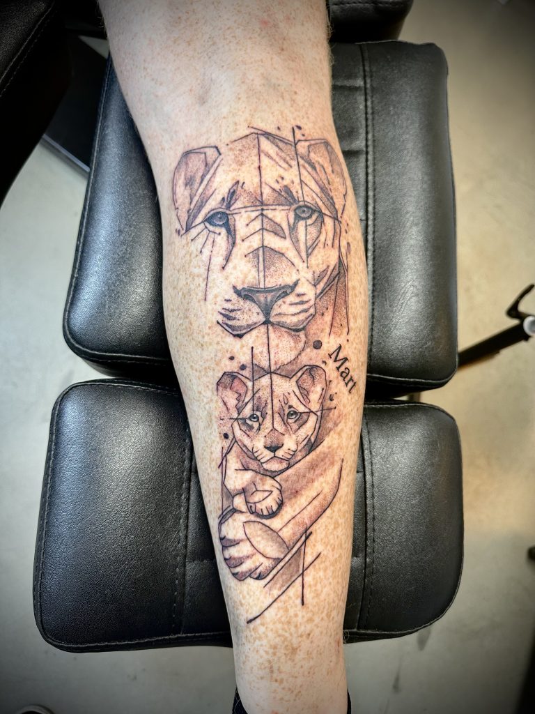 Geometrische leeuwin en welp tattoo op onderbeen met naam 'Mart'.