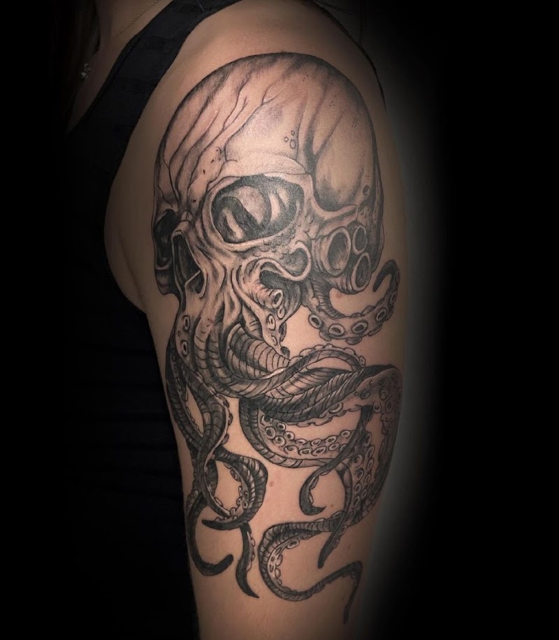 Zwart-wit tattoo van een schedel met octopus tentakels op de bovenarm.