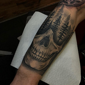 Realistische schedel die overgaat in een dennenbos op het onderbeen.