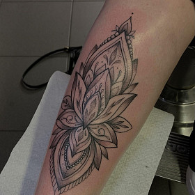 Sierlijke mandala-stijl lotusbloem op onderbeen, zwart-wit.