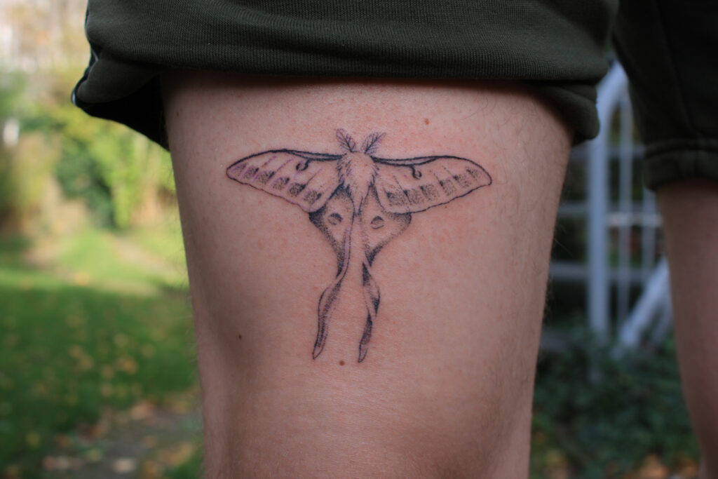 Gedetailleerde fineline mot tattoo op het bovenbeen.