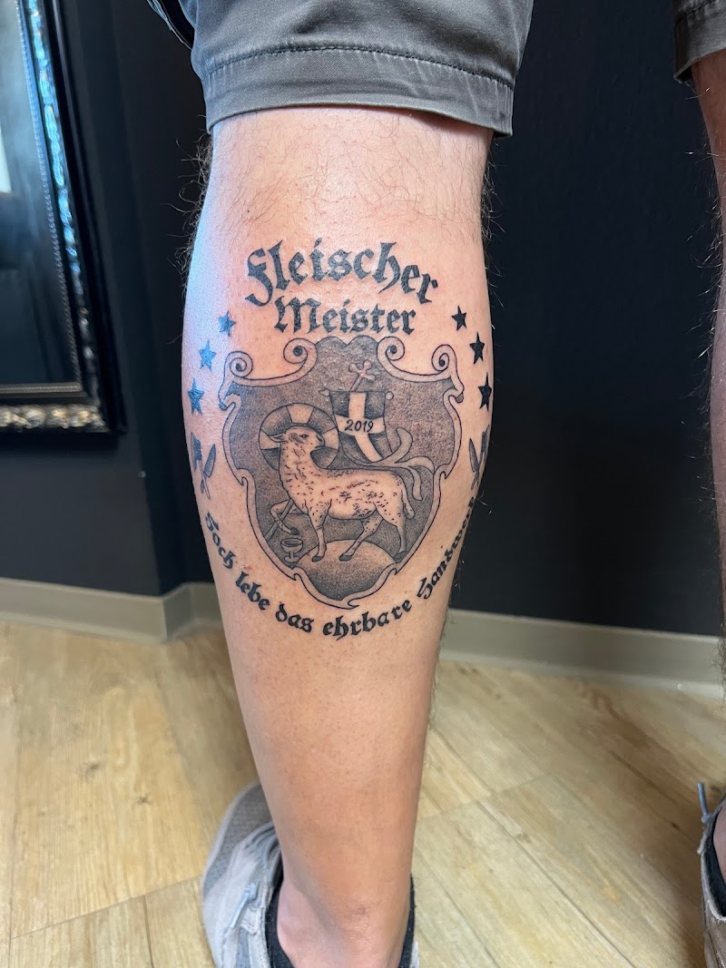 Zwart-wit wapenschild tattoo met lam, tekst 'Fleischer Meister' en jaartal 2019.