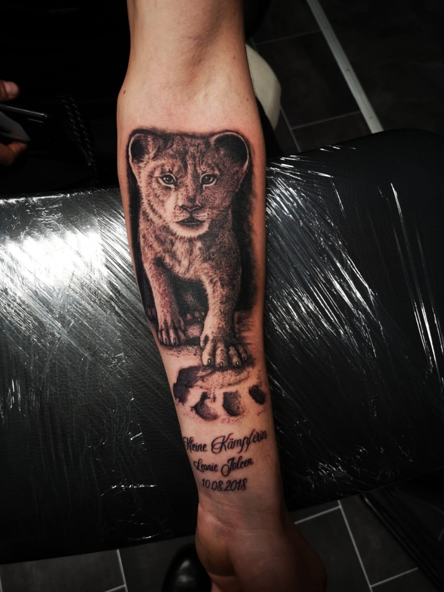 Realistische leeuwenwelp met pootafdruk en tekst op onderarm.