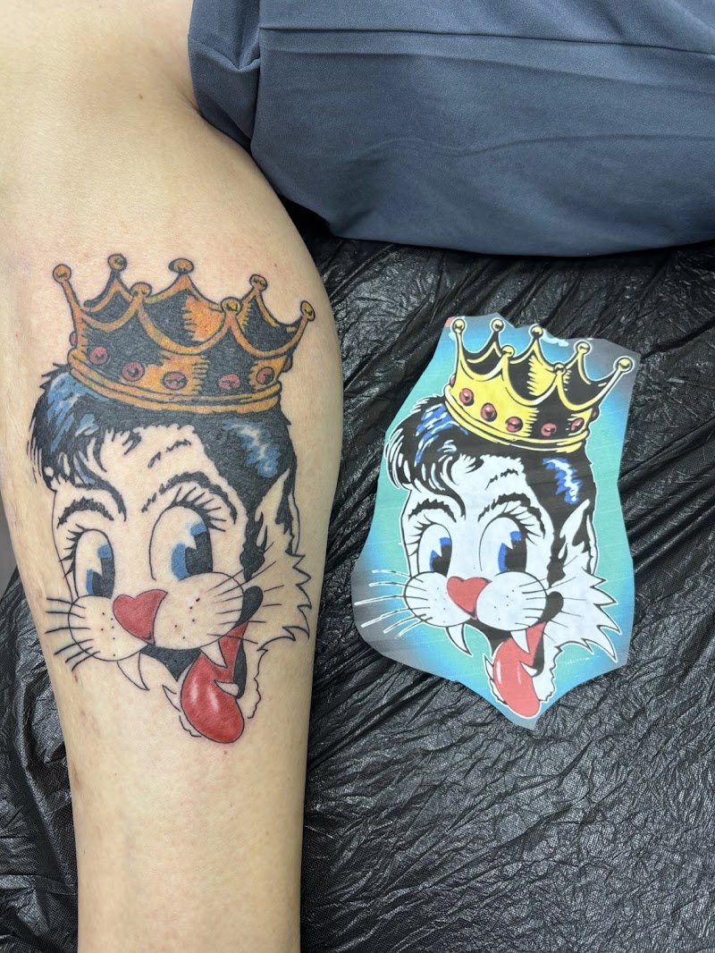 Traditional tattoo van een kattenkop met een kroon en tong uit.