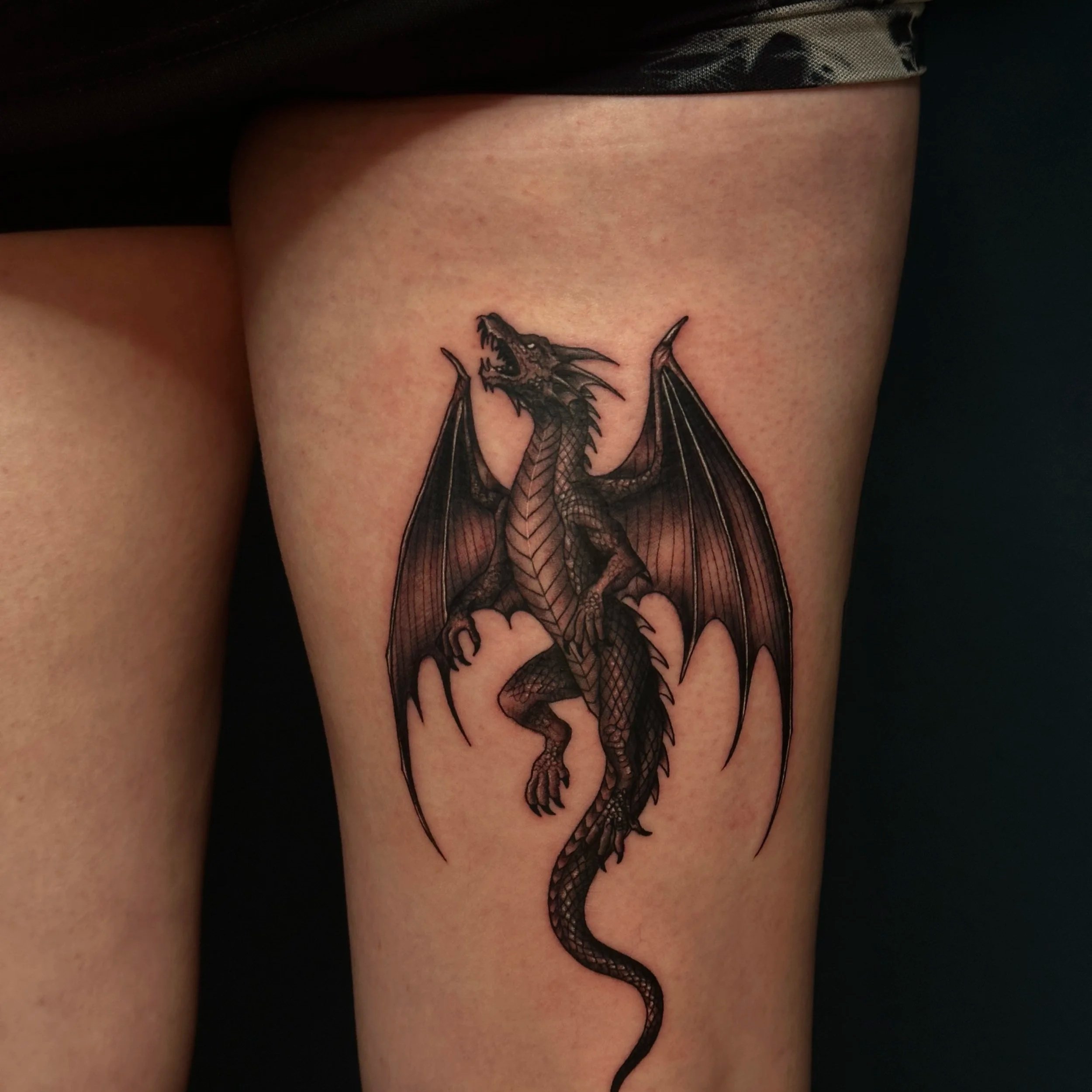 Gedetailleerde zwart-wit draak tattoo op het bovenbeen.