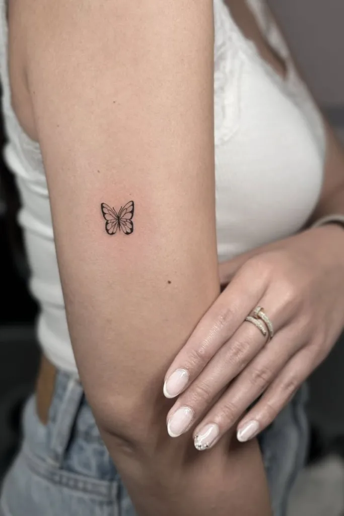 Kleine, minimalistische vlinder tattoo op de bovenarm.
