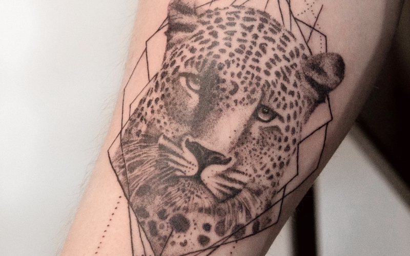 Realistische luipaardkop met geometrische lijnen op onderarm.