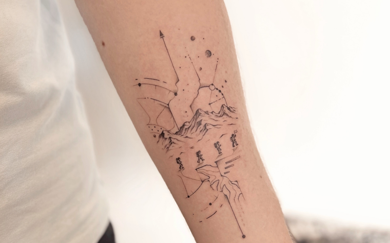 Fineline tattoo van bergbeklimmers, bergen en sterrenbeelden op de onderarm.