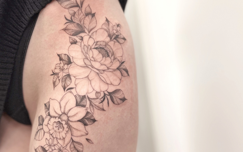 Fineline bloemen tattoo op bovenbeen, pioenroos en narcis.