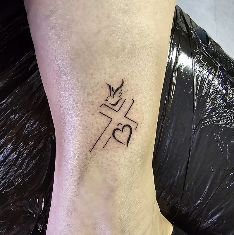 Minimalistische fineline tattoo van een kruis, hart en duif op de enkel.