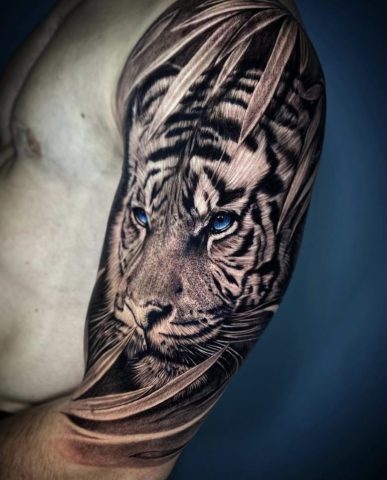 Realistische tijger met blauwe ogen tussen bladeren op bovenarm.