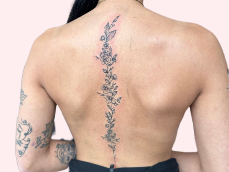 Fineline bloemenrank tattoo langs de ruggengraat.
