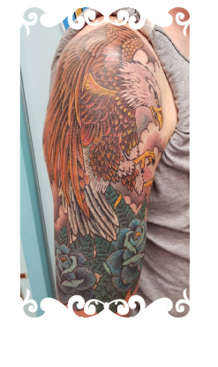 Traditionele tattoo van een adelaar en blauwe rozen op de bovenarm.