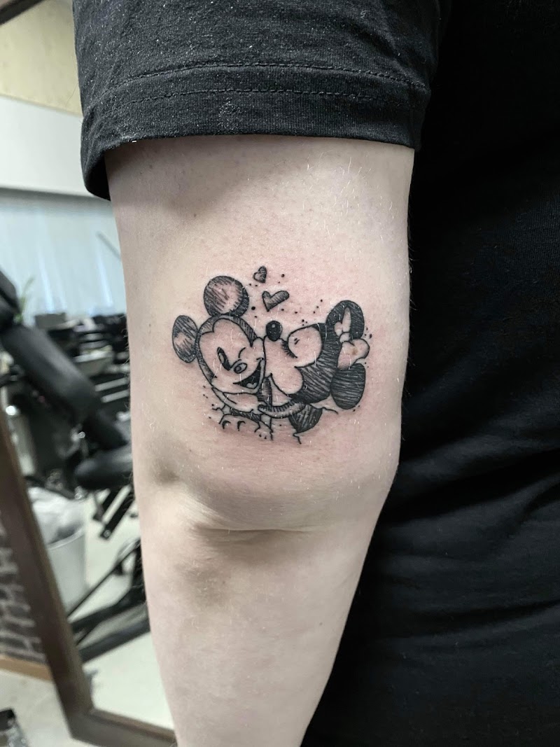 Schetsstijl tattoo van kussende Mickey en Minnie Mouse met hartjes op bovenarm.
