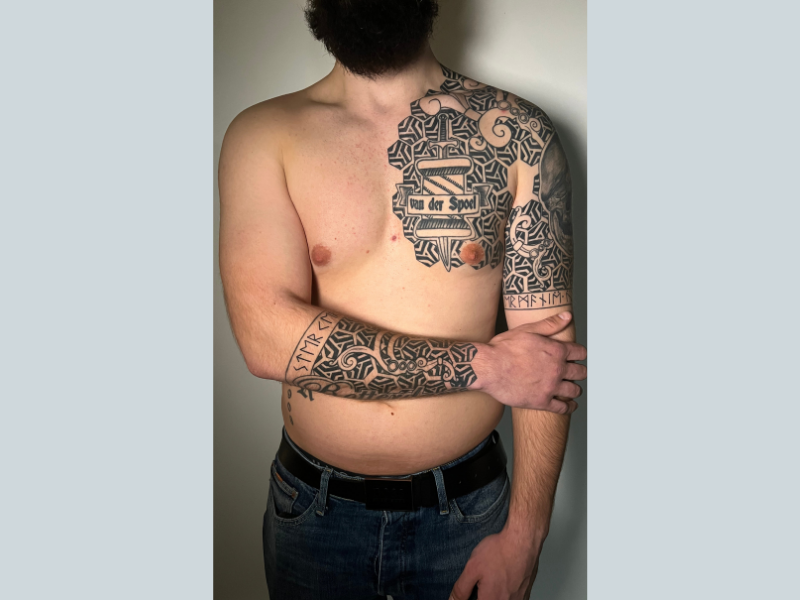 Grote geometrische en Noorse tattoo op borst en arm, met tekst en runen.