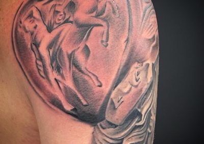 Realistische zwart-wit tattoo van een ruiter te paard in reliëf op de schouder.