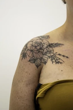 Blackwork bloemen tattoo op schouder met rozen en bladeren.