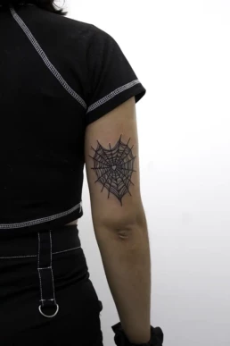 Zwartwerk spinnenweb tattoo in hartvorm op de achterkant van de bovenarm.