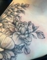 Fineline bloementattoo met pioenroos en bladeren op schouder.
