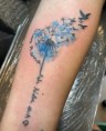 Blauwe aquarel paardenbloem met vogels en tekst "life is like a..." op onderarm.