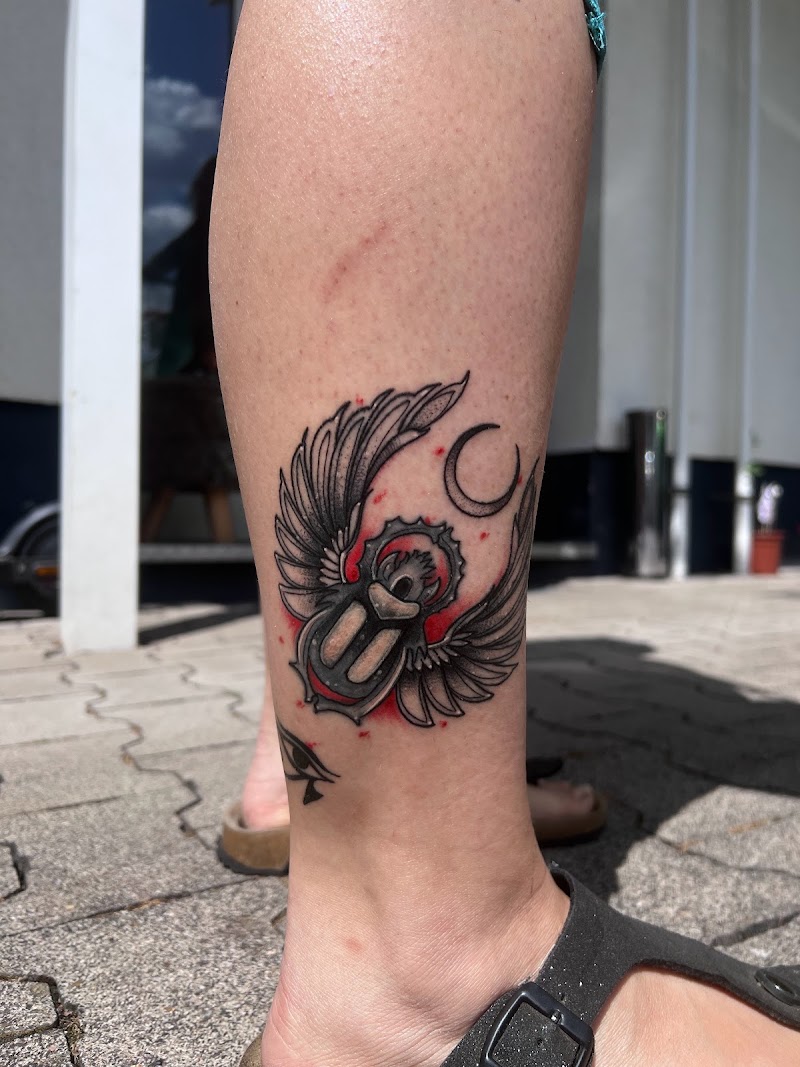 Gevleugelde scarabee met maansikkel en rode accenten op onderbeen.