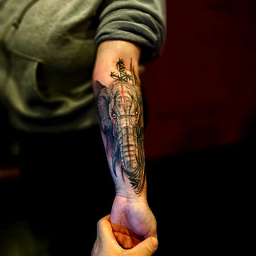 Realistische olifant met rode streep en geometrische patronen op onderarm.