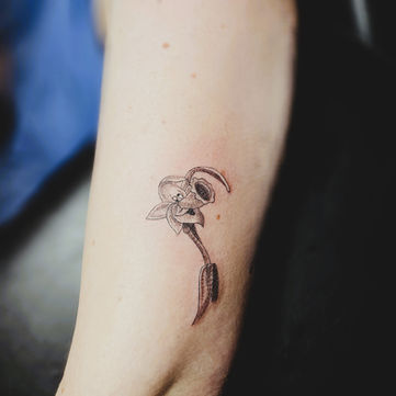 Fineline tattoo van een verwelkte bloem op de onderarm.